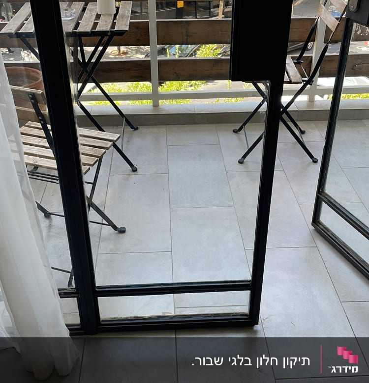 דלת זכוכית פתוחה למרפסת עם שולחן וכיסאות